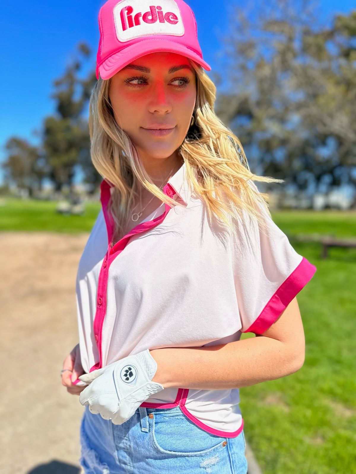 Pink Caddy Camp golf shirt on a model also wearing a pink Pirdie golf trucker hat and jean shorts on a golf course.