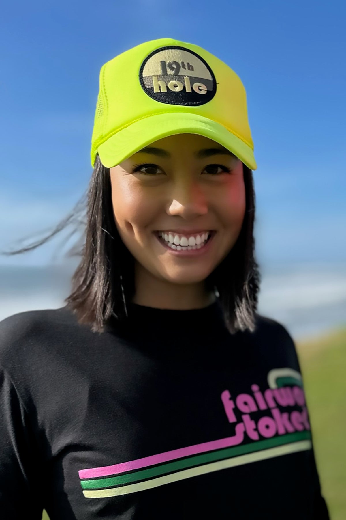 Model wearing neon yellow 19th hole golf trucker hat.