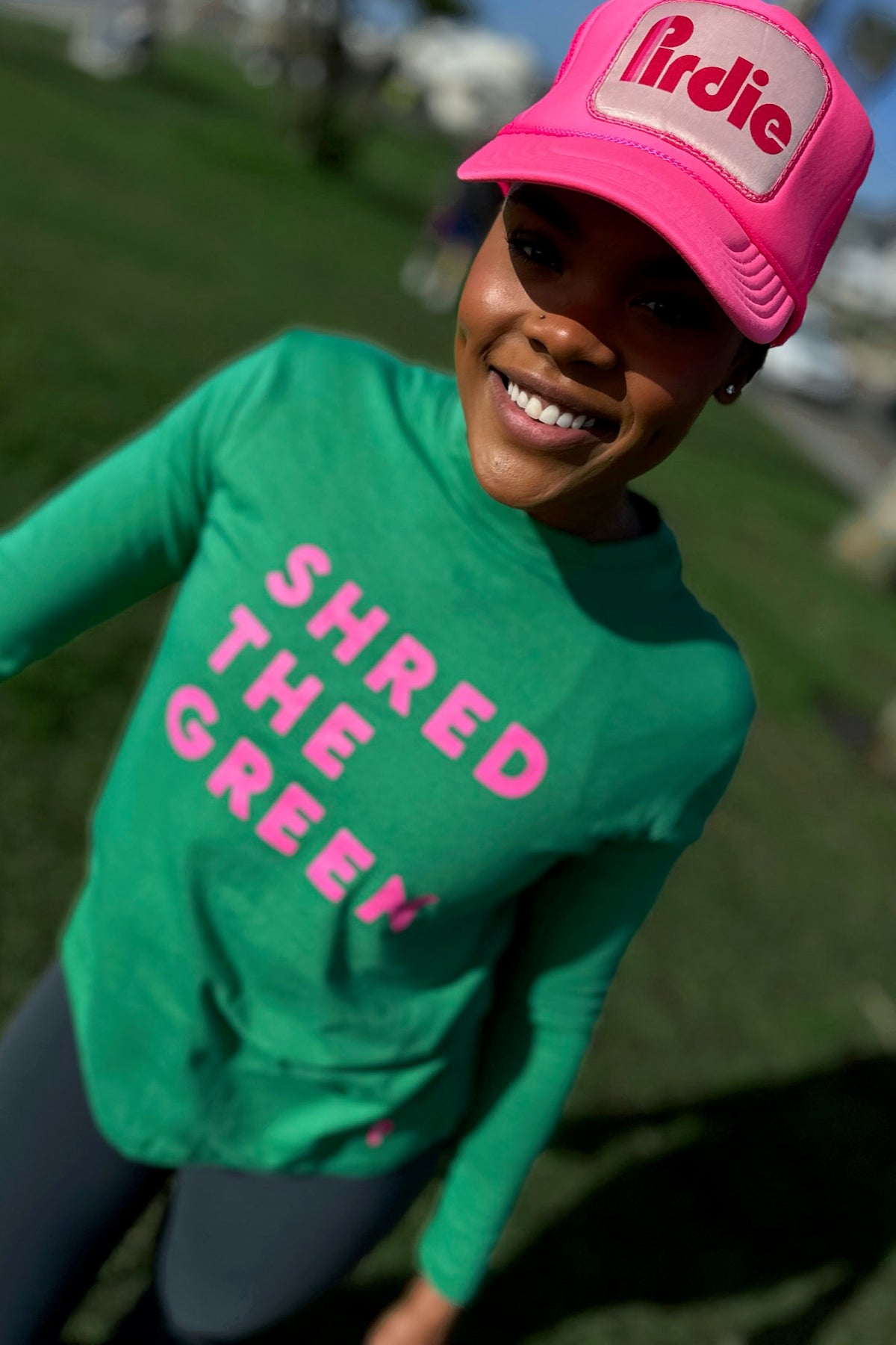 Model wearing Shred the Green women's longsleeve golf shirt and pink Pirdie golf trucker hat