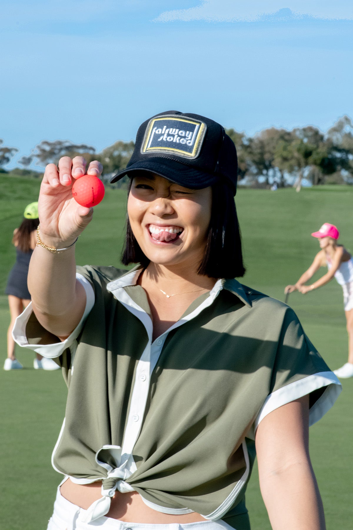 Model wearing black Fairway Stoked golf trucker hat  on a golf course holding a golf ball.